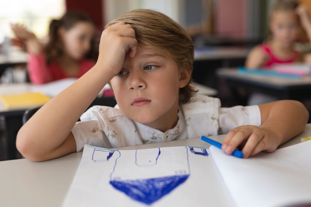 sad schoolboy studying in classroom sitting at desks in school