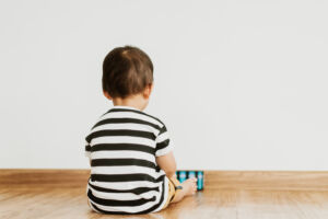 back view of little baby boy sitting alone and watching smartpho